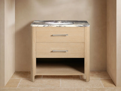 Calista Single Vanity with oak wood finish, marble stone top, ceramic sink, dual silver handles, open shelf with towels.