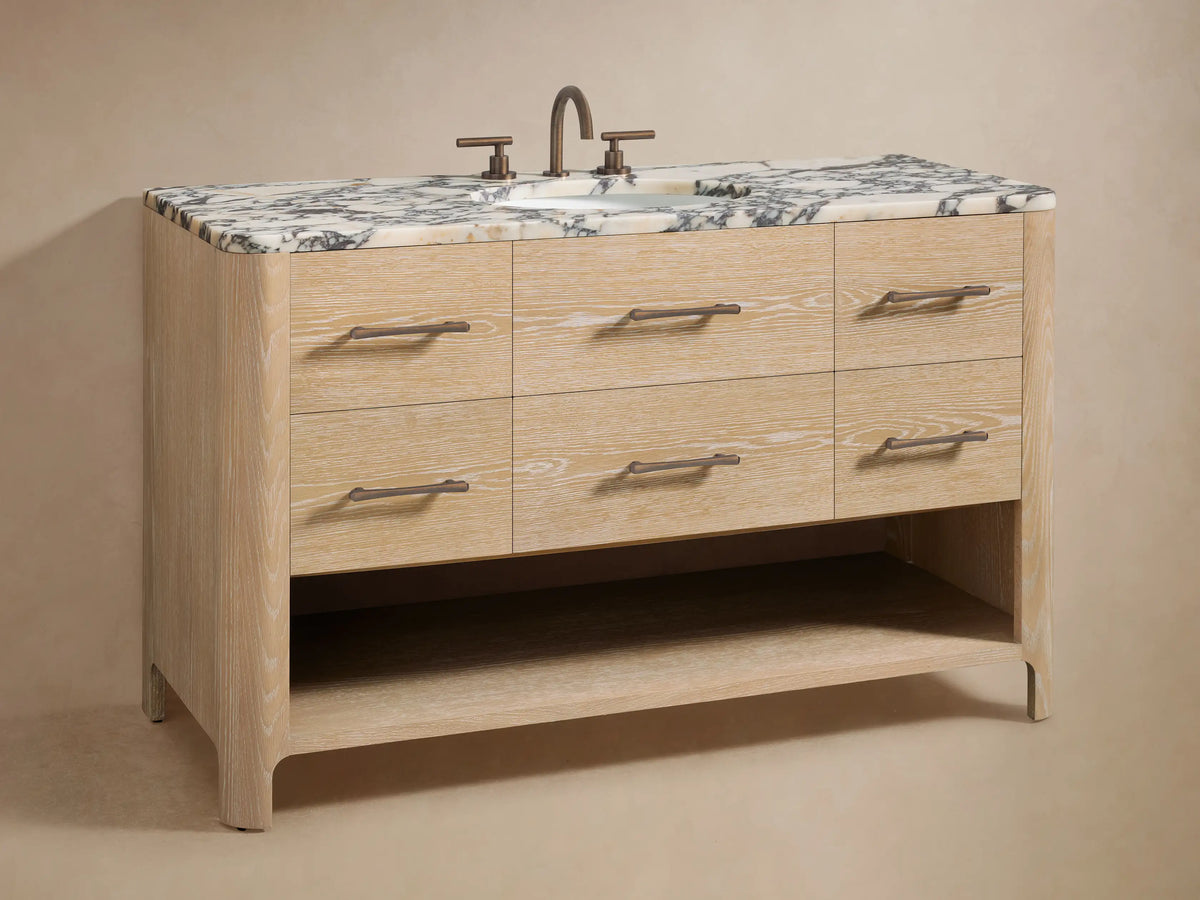 Close-up of light oak Calista Wide Single Vanity. Two drawers slightly open reveal rolled white towels, bottles, wooden organizers. Dark bronze handles.