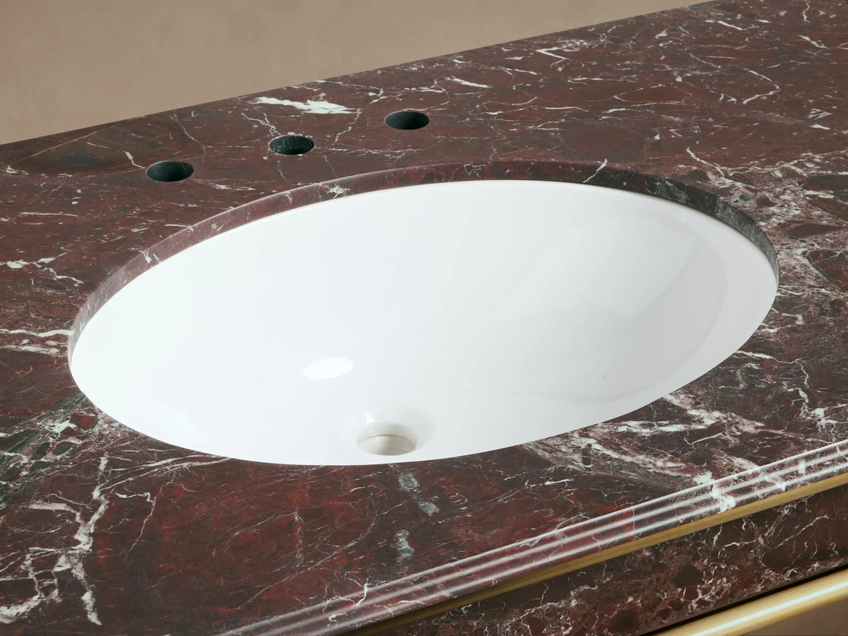 Close-up of Chelsea Washstand sink. White oval ceramic sink in red Levanto marble countertop with antique brass faucet.