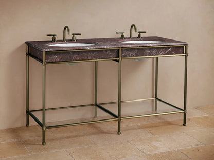 Chelsea Double Washstand. Red Levanto marble top with two white oval sinks. Antique brass frame, lower glass shelf, against a tan wall.