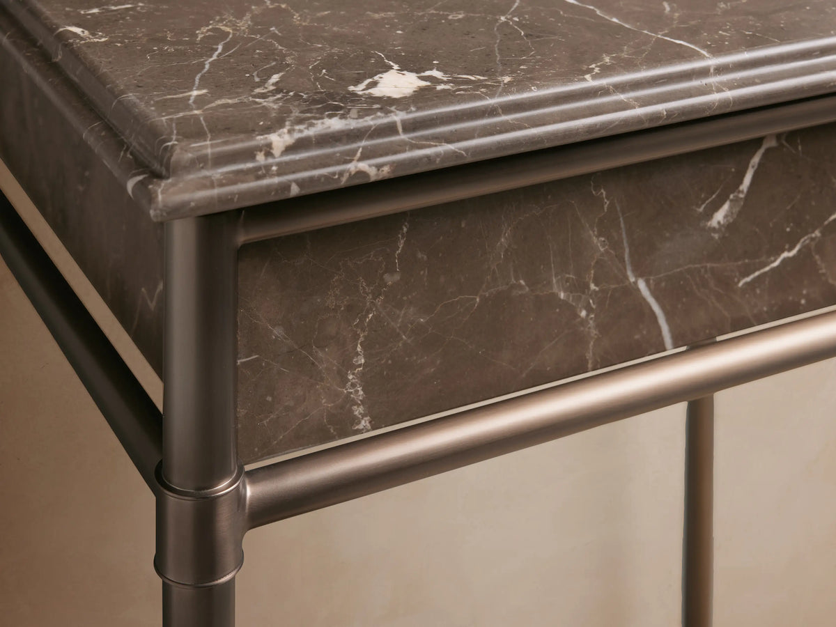 Lower glass shelf of Chelsea Powder Washstand in bronze finish, with folded beige towels, amber bottle, and jar.