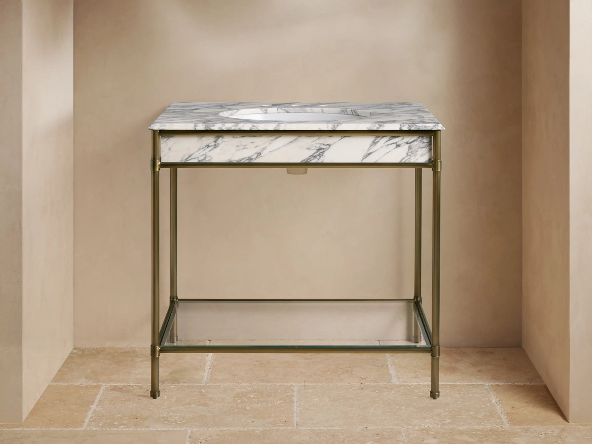 Chelsea Single Washstand: White veined marble top, undermount sink, gold widespread faucet, antique brass frame, glass shelf with towels.