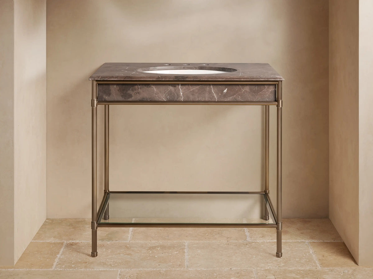Chelsea Single Washstand: dark brown marble top, white oval sink, antique bronze frame, glass shelf with towels & decor.