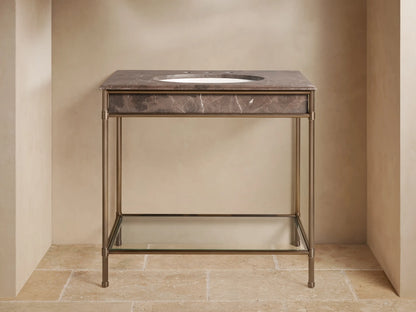 Chelsea Single Washstand: dark brown marble top, white oval sink, antique bronze frame, glass shelf with towels & decor.