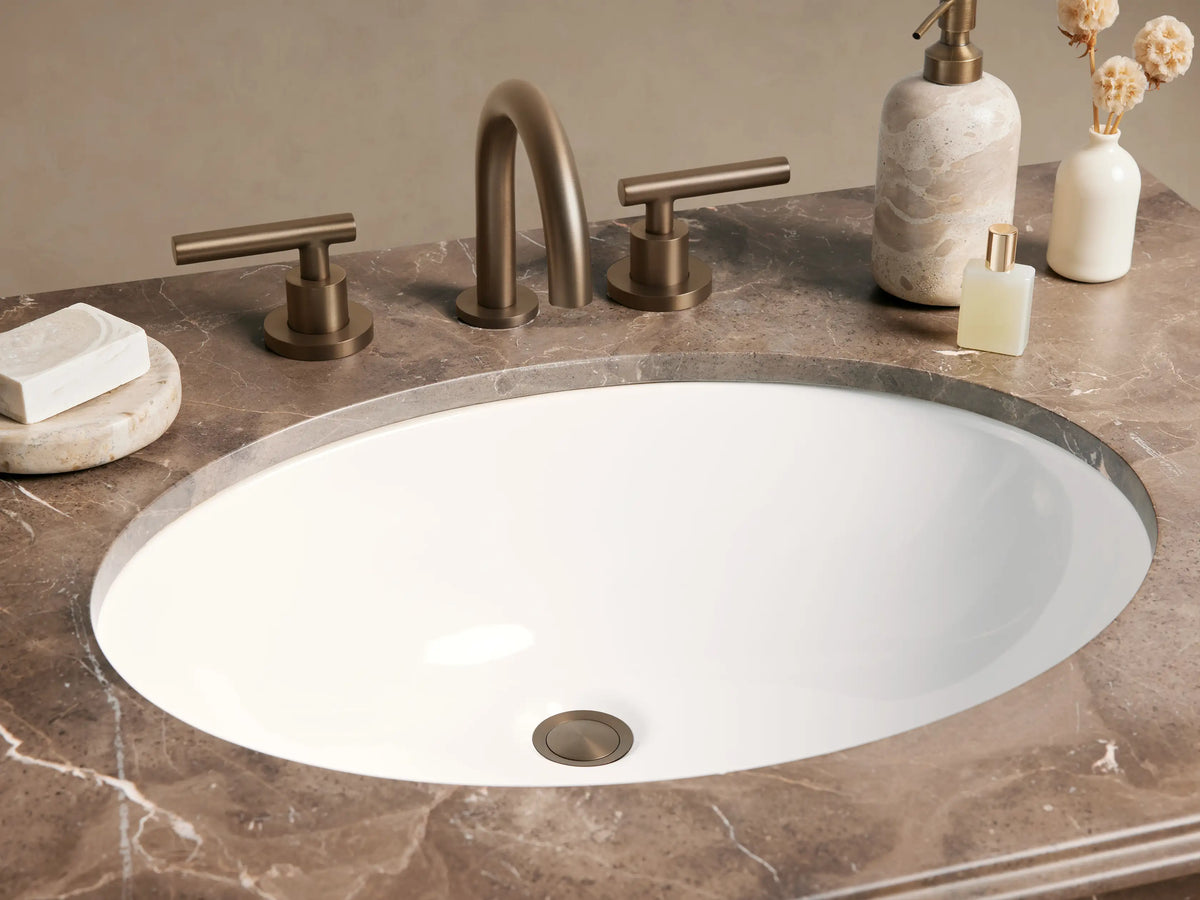 Chelsea Single Washstand with dark brown marble top, white oval sink, antique bronze frame, and glass shelf, in a room.