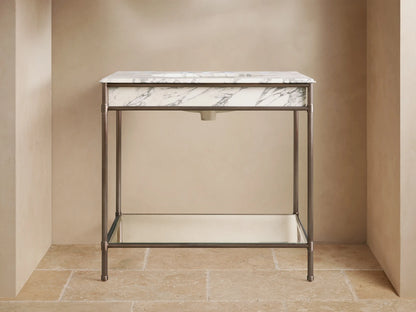Chelsea Single Washstand with an antique bronze frame, white Carrara marble top, undermount sink, and glass shelf holding white towels.