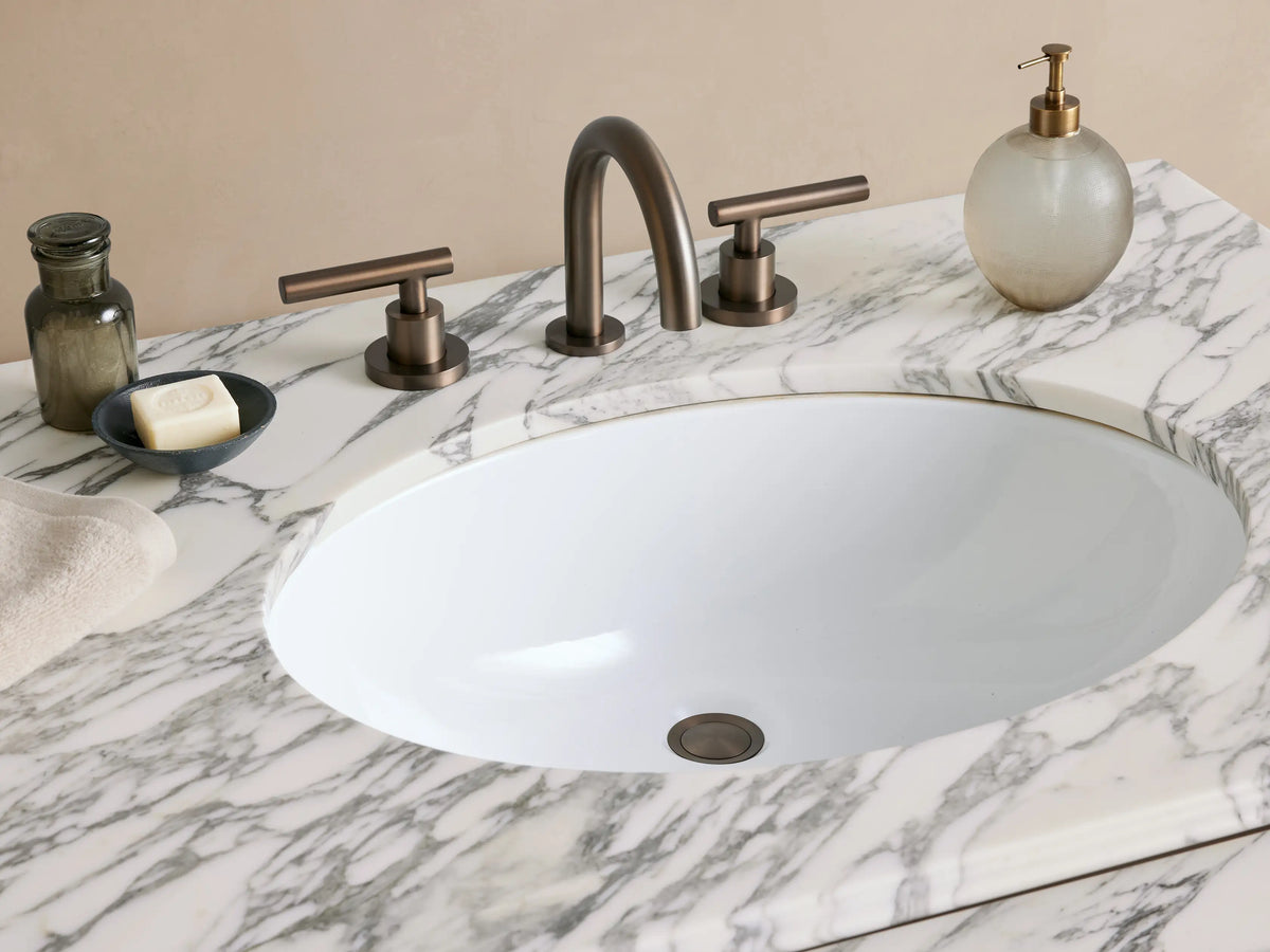Chelsea Single Washstand with white veined marble top, undermount sink, antique bronze metal frame & glass shelf on tiled floor.