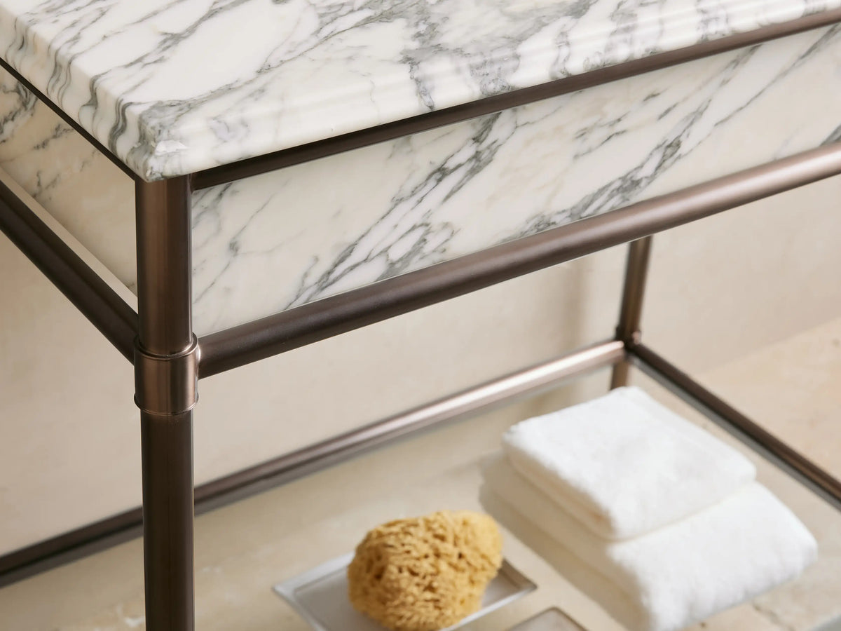 Chelsea Single Washstand close-up: white oval ceramic undermount sink in a white marble countertop with grey veins & 3 faucet holes.
