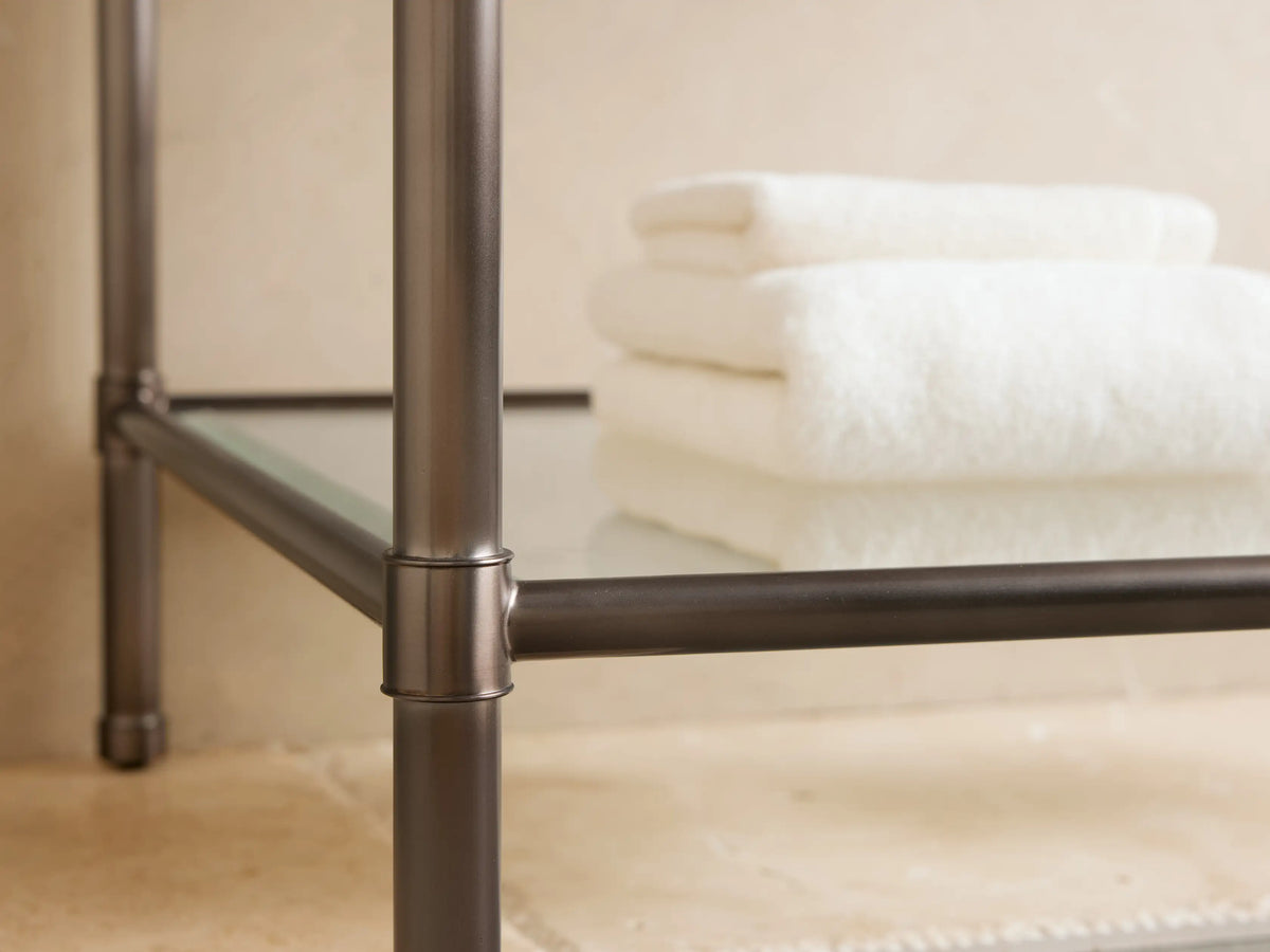 Chelsea Single Washstand: white marble top with grey veins, Antique Bronze frame, glass shelf with white towels and sponge.