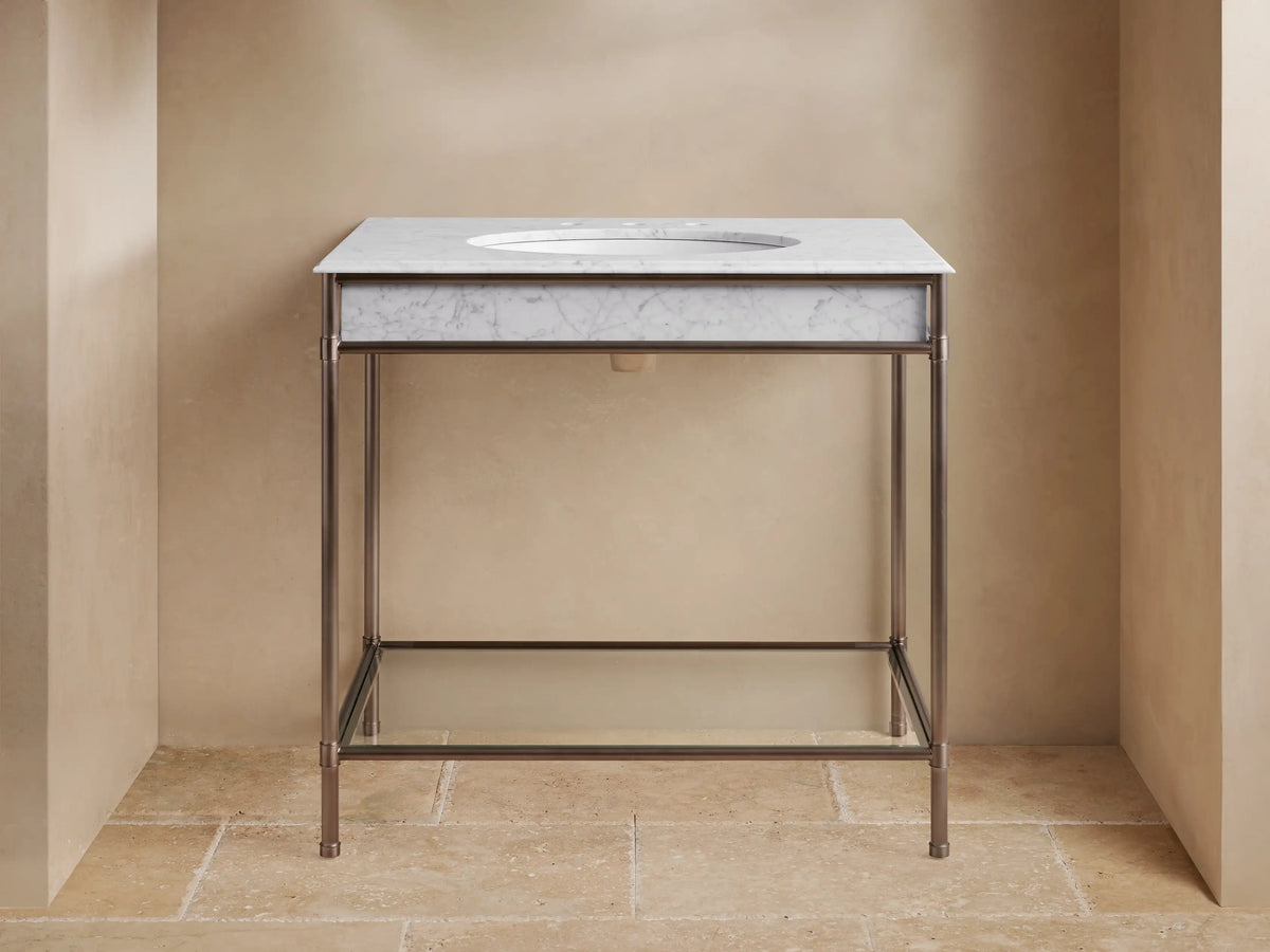 Chelsea Single Washstand with dark bronze frame, white veined marble top, oval sink, glass shelf, decorated with towels, candles.