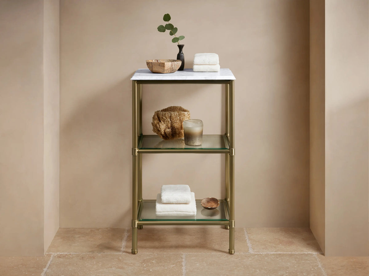 Chelsea Short Etagere with antique brass frame, Carrara marble top, two glass shelves, and decorative items in a beige setting.