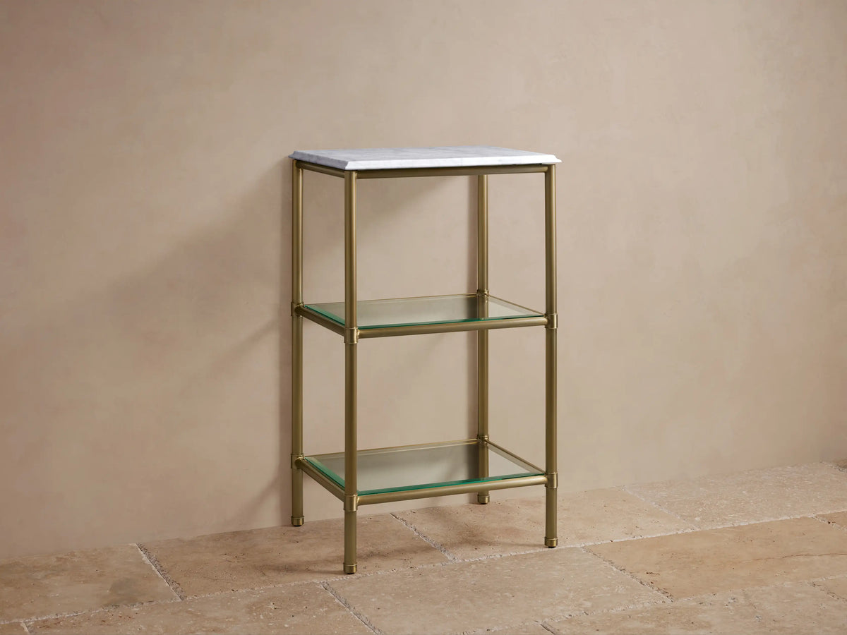 Chelsea Short Etagere with antique brass frame, Carrara marble top, two glass shelves, and decorative items in a beige setting.