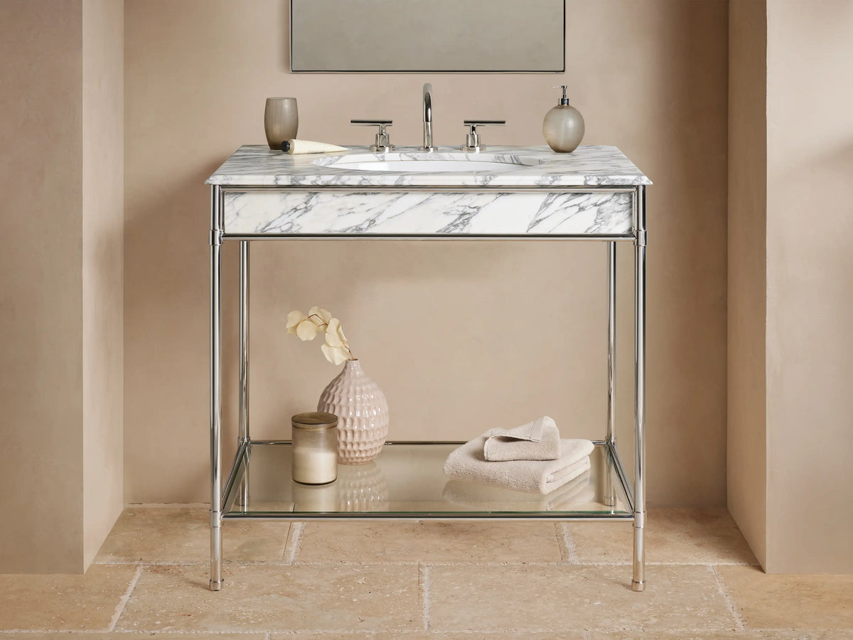 Chelsea Single Washstand: polished nickel frame, white marble top, oval sink, glass shelf with vase & towels, on beige floor.