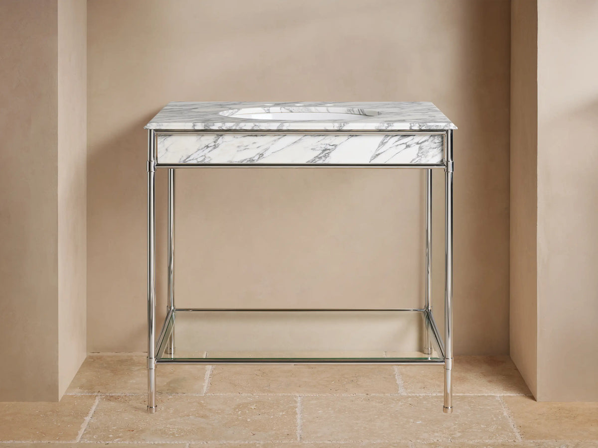 Chelsea Single Washstand: polished nickel frame, white marble top, oval sink, glass shelf with vase & towels, on beige floor.