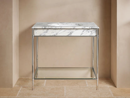 Chelsea Single Washstand: polished nickel frame, white marble top, oval sink, glass shelf with vase & towels, on beige floor.
