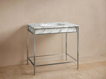Chelsea Single Washstand: Polished nickel frame, white marble top with grey veins, oval sink, faucet, lower shelf, beige room.