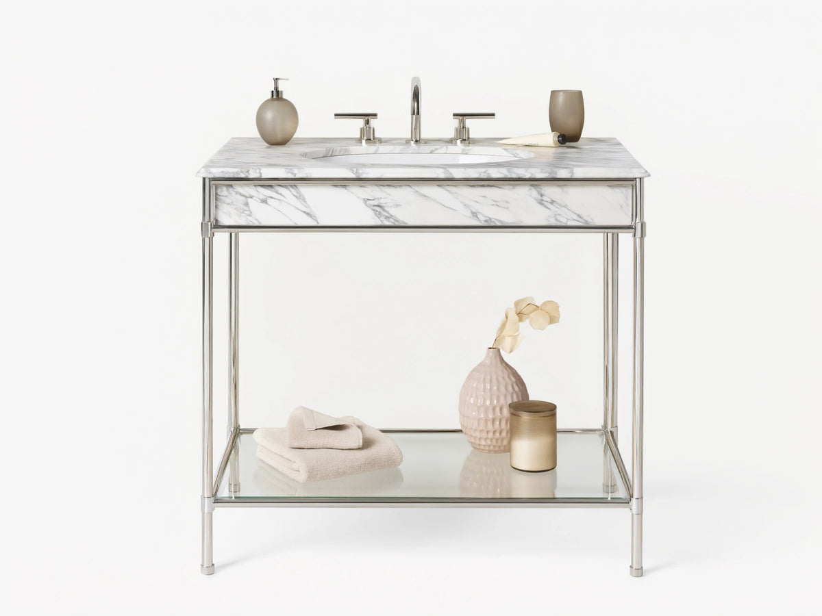 Chelsea Single Washstand: polished nickel frame, white marble top, oval sink, glass shelf with vase & towels, on beige floor.