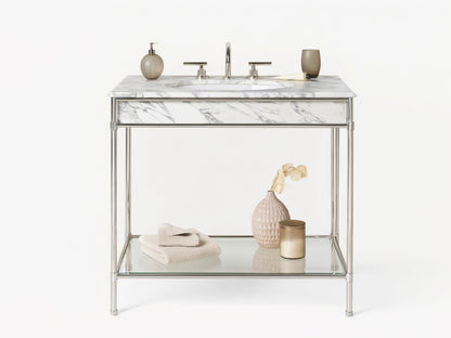 Chelsea Single Washstand: polished nickel frame, white marble top, oval sink, glass shelf with vase & towels, on beige floor.