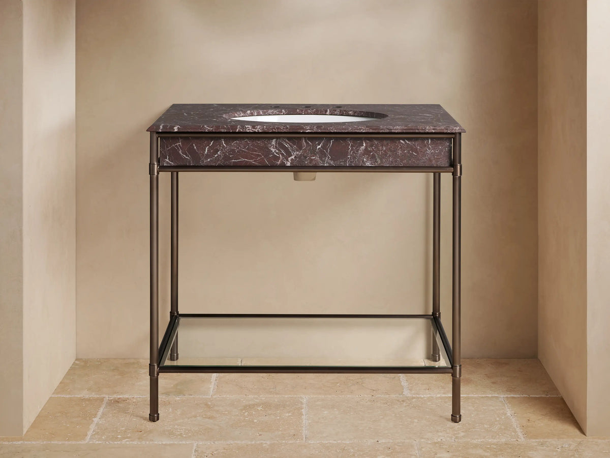 Chelsea Single Washstand, Red Levanto marble top, white oval sink, antique bronze frame, glass shelf with towels, bathroom setting.