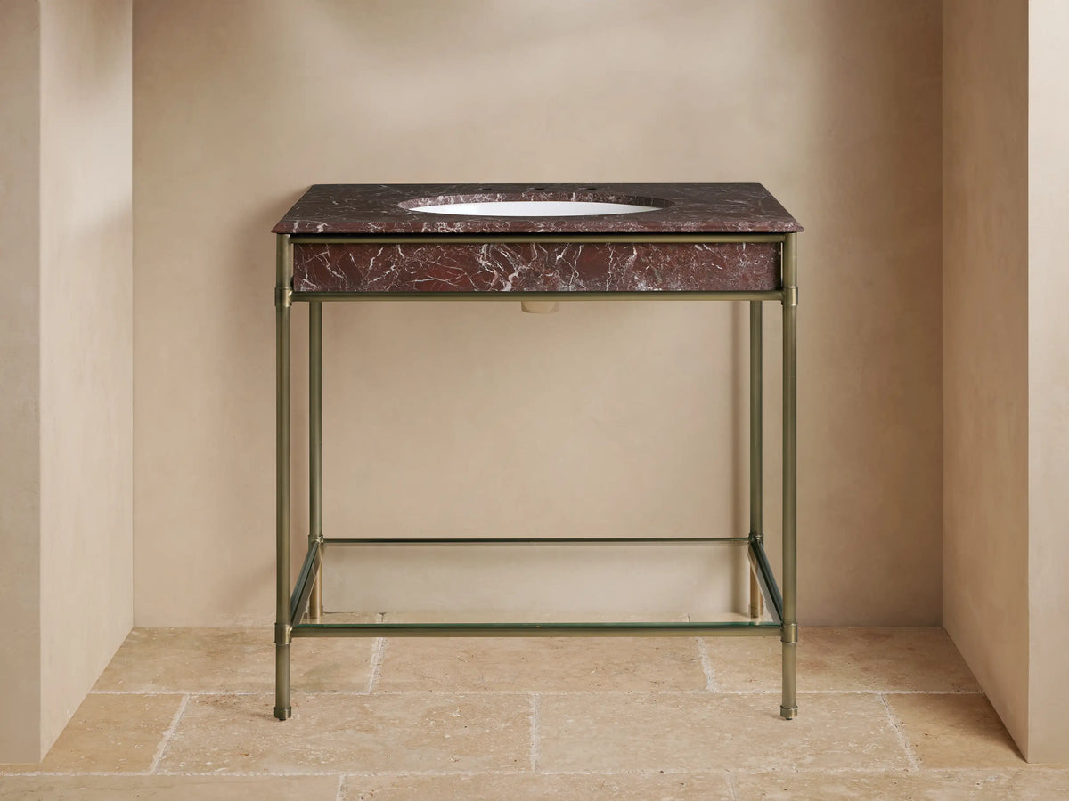 Chelsea Single Washstand with a Red Levanto marble top, white oval sink, and brass faucet on an antique brass frame, glass shelf below with towels.
