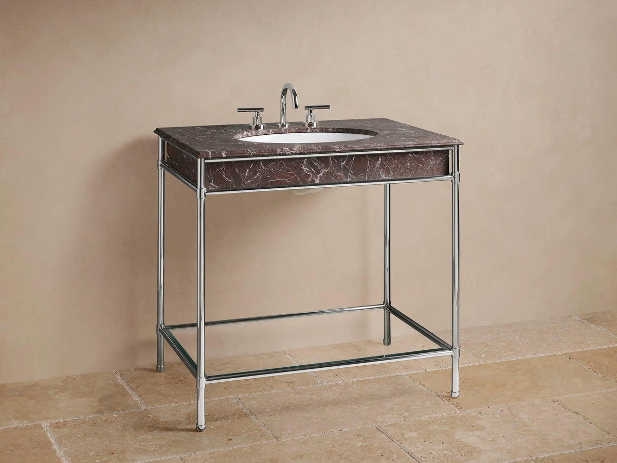 Chelsea Single Washstand close-up: polished nickel frame, glass shelf with a beige textured vase, candle, and folded towels.