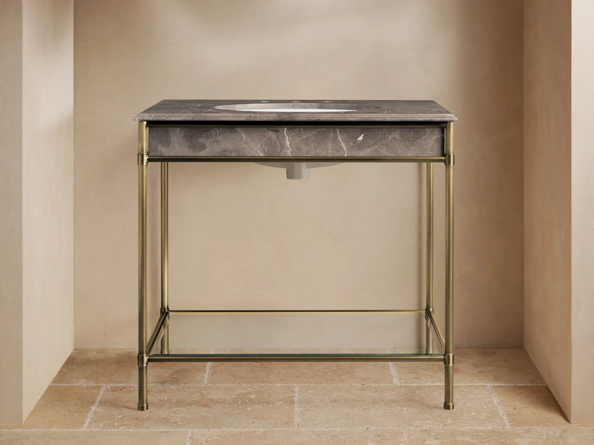 Chelsea Single Washstand, front view. Dark gray veined marble top with brass faucet, brass frame, and glass shelf with towels.