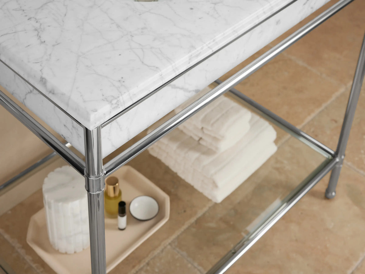 Chelsea Single Washstand: Close-up of white oval sink, polished nickel faucet on white marble with grey veins. Green soap & sprigs in background.