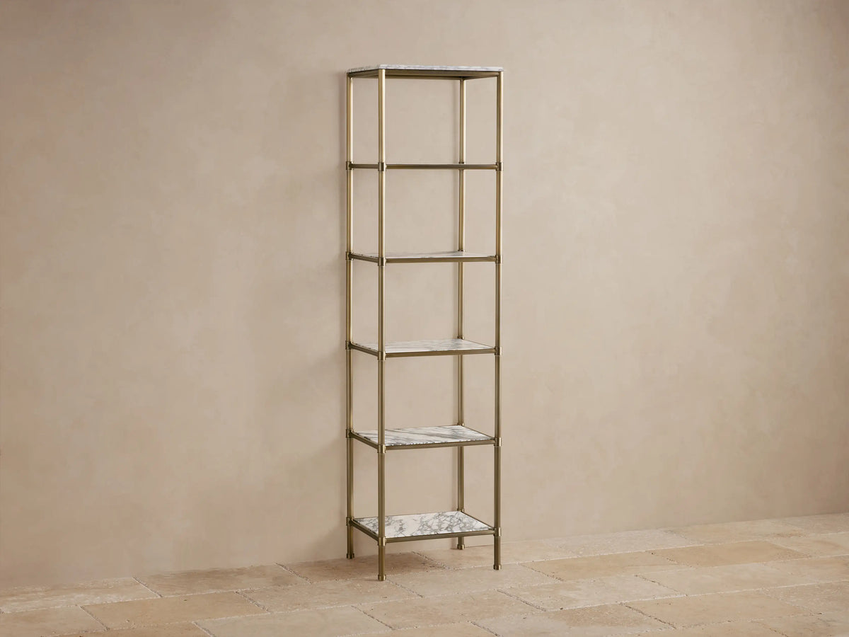 Chelsea Tall Etagere with antique brass frame, 5 white marble shelves, styled with vase, jars & towels, against beige wall.