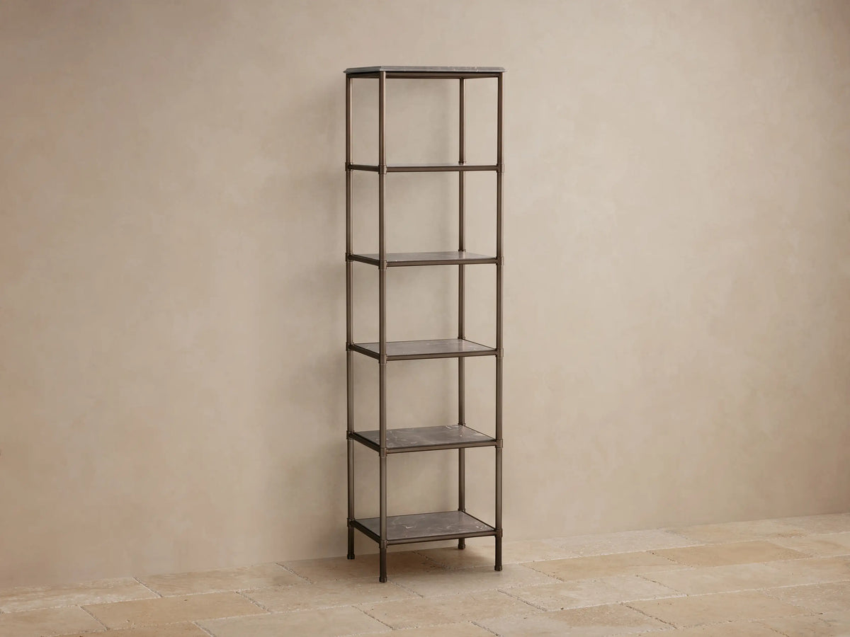Chelsea Tall Etagere: Antique bronze etagere with 5 gray marble shelves holding toiletries, towels, & decor, against a beige wall.