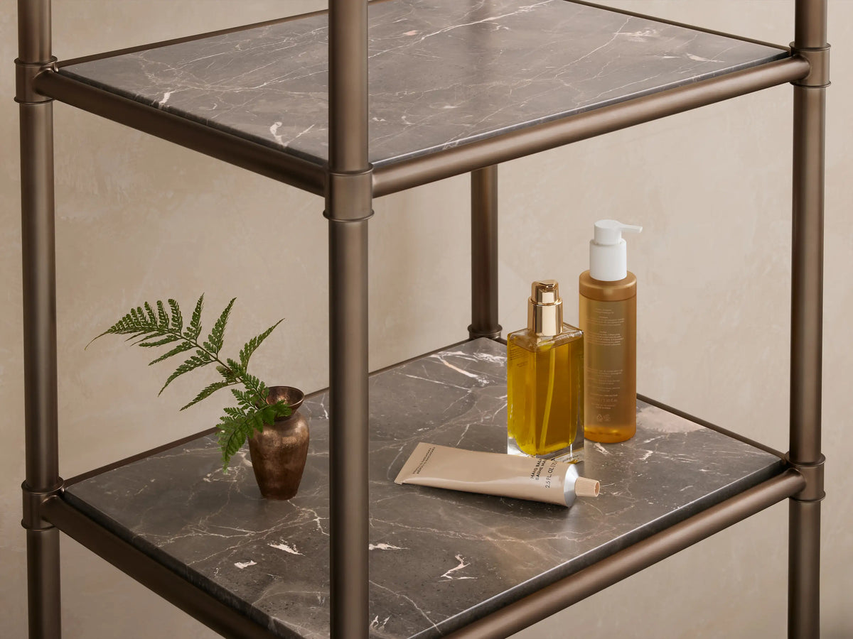 Chelsea Tall Etagere with an antique brass metal frame and five dark, patterned marble shelves, against a beige wall.