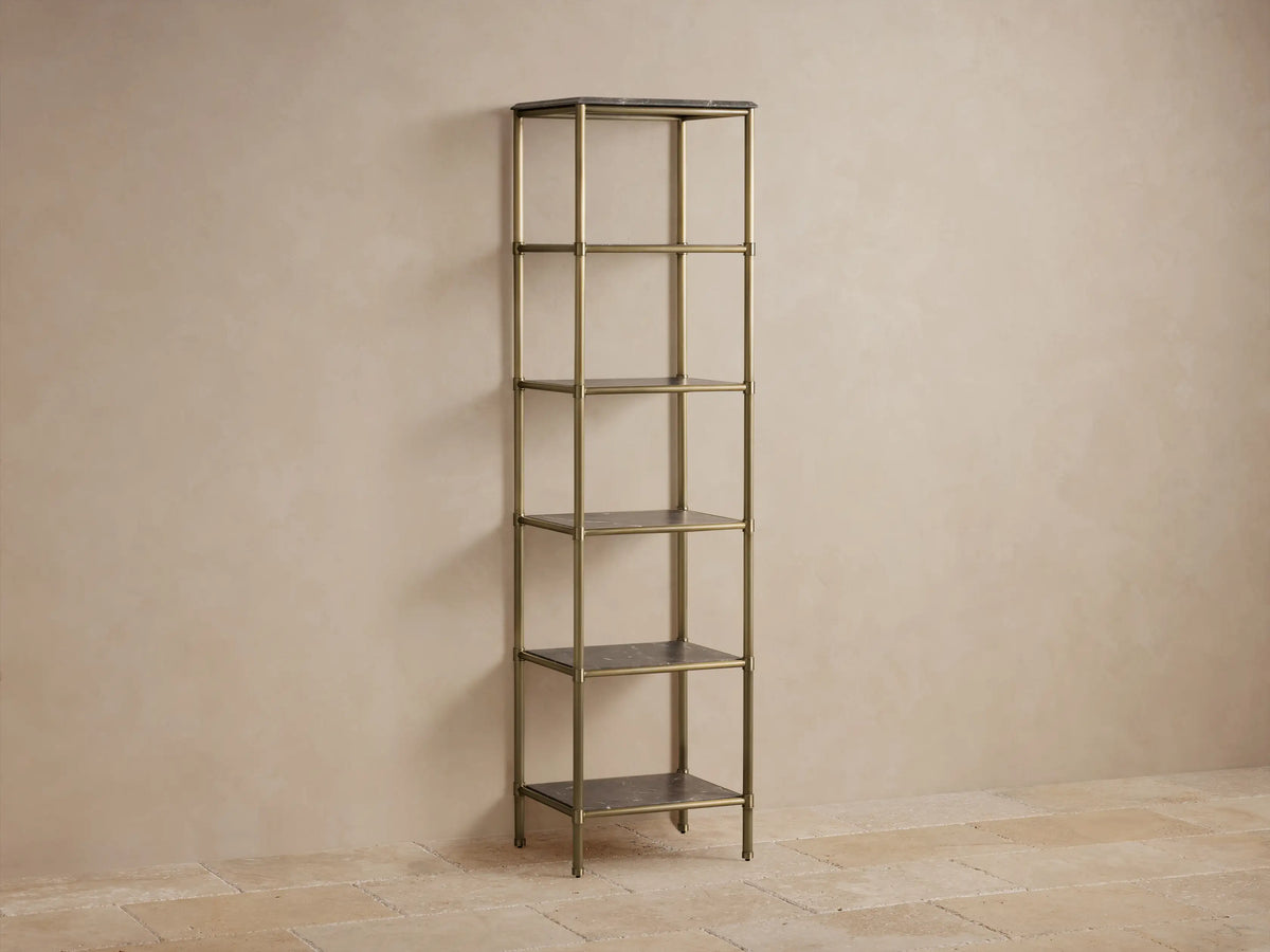 Tall five-shelf Chelsea Etagere with an antique brass finish and marble shelves, holds decor items against a beige wall.