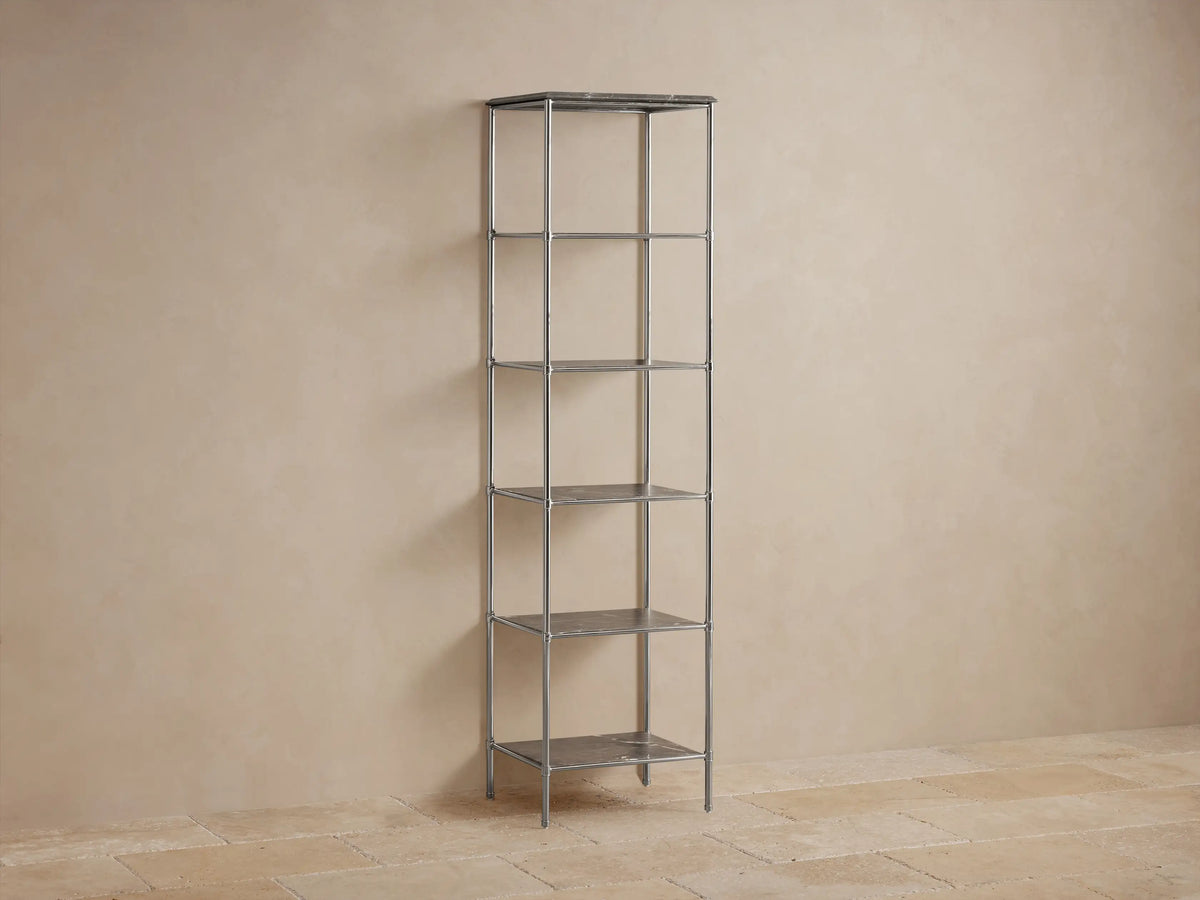 Chelsea Tall Etagere in polished nickel finish with five open shelves, stone top, displaying decor and rolled towels against a beige wall.