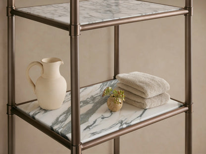 Chelsea Tall Etagere with dark antique bronze frame, 5 honed white marble shelves with gray veining, standing against a beige wall.