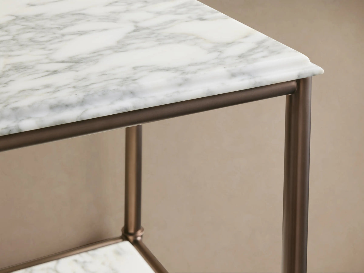 Chelsea Tall Etagere, close-up. Antique brass frame, white marble shelves with gray veins. Beige pitcher, towels, plant on lower shelf.
