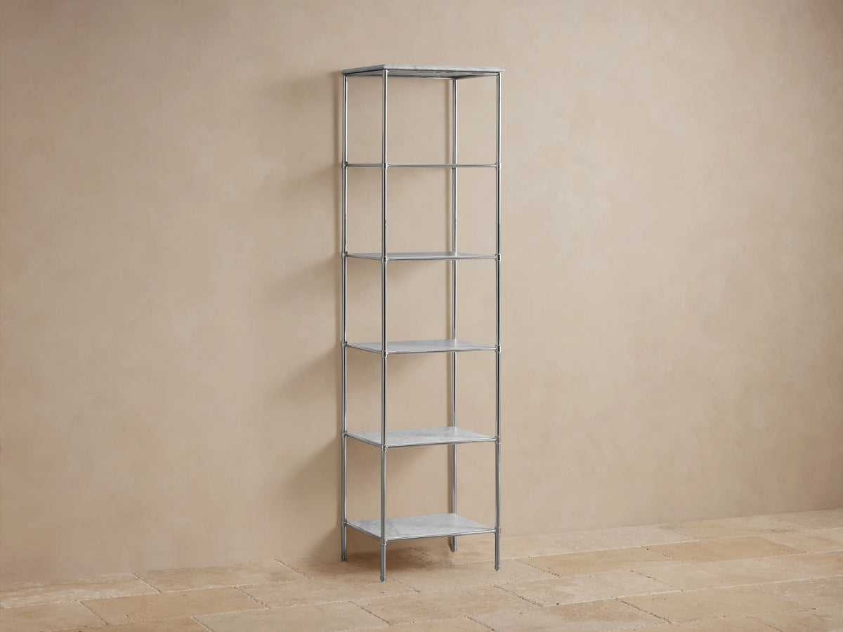 Chelsea Tall Etagere made of stainless steel in polished nickel finish, featuring five shelves with decorative items and towels, against a beige wall.