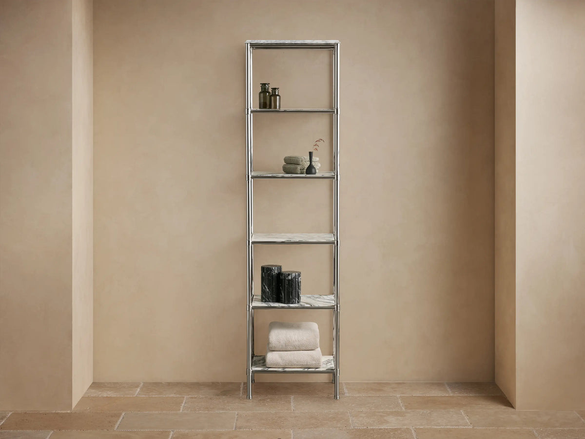 Chelsea Tall Etagere, polished nickel frame, 5 veined marble shelves, displaying towels, bottles, vases in a beige room.