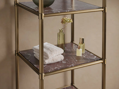 Chelsea Tall Etagere with an antique brass frame and 5 dark, veined marble shelves, standing against a beige wall on stone tiles.