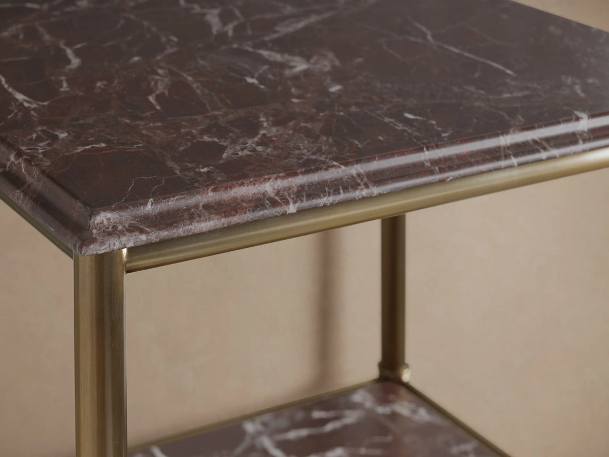 Chelsea Tall Etagere, close-up, showing antique bronze frame and dark red marble shelves with white veining, styled with towels, vase & bottles.