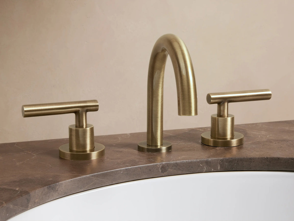 Crewe Smooth Faucet in antique brass with curved spout and two cylindrical handles on a light countertop.