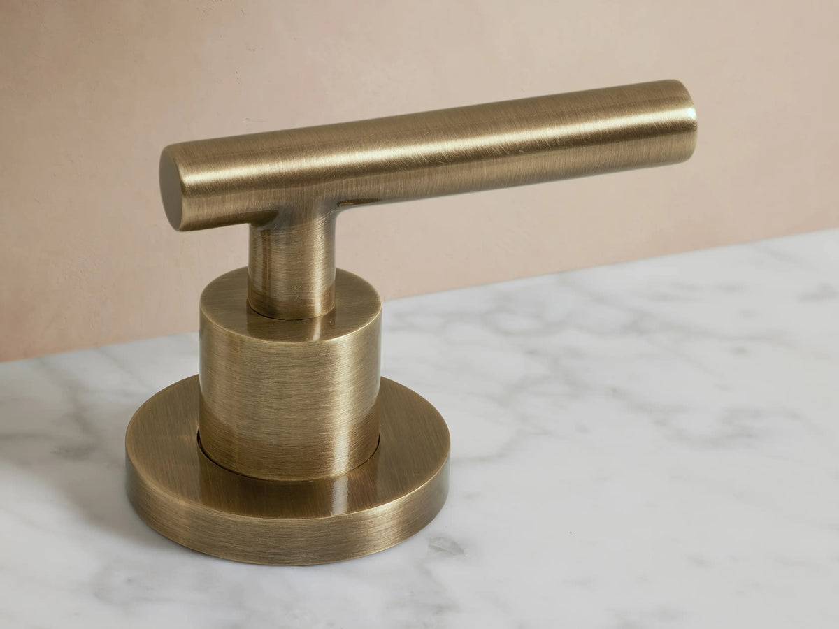 Crewe Smooth Faucet in antique brass finish on a marble countertop, featuring two cylindrical handles and a curved spout over a sink.