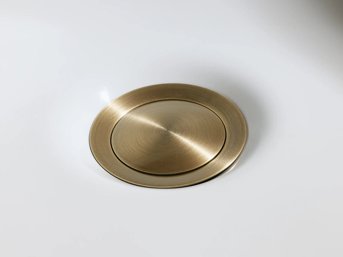 Crewe Smooth Faucet handle shown in antique brass finish on a marble surface, featuring rounded, cylindrical design.