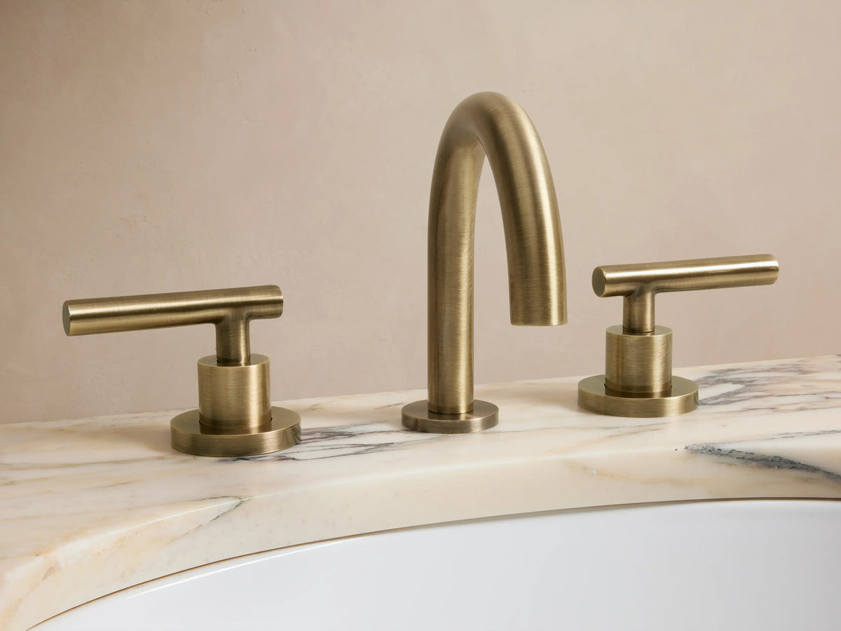 Crewe Smooth Faucet in antique brass finish, showing two cylindrical handles and a curved spout on a dark countertop.