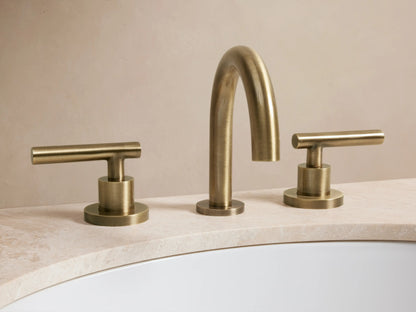 Crewe Smooth Faucet in antique brass finish with arched spout and two horizontal cylindrical handles on marble countertop.