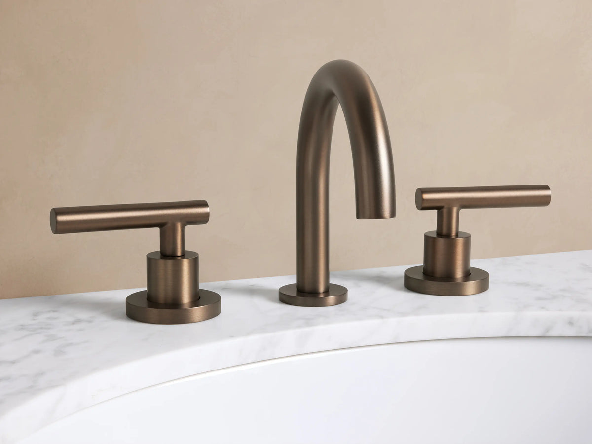 Crewe Smooth Faucet in Antique Bronze, with an arched spout and two smooth T-bar handles on a white marble counter.