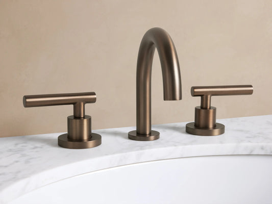 Crewe Smooth Faucet in Antique Bronze, with an arched spout and two smooth T-bar handles on a white marble counter.