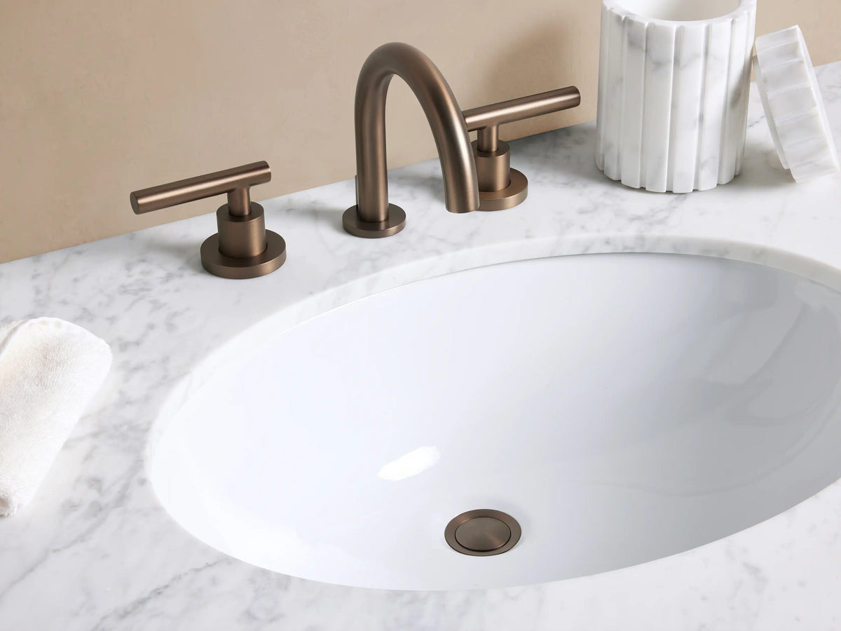 Crewe Smooth Faucet in Antique Bronze, with an arched spout and two smooth T-bar handles on a white marble counter.