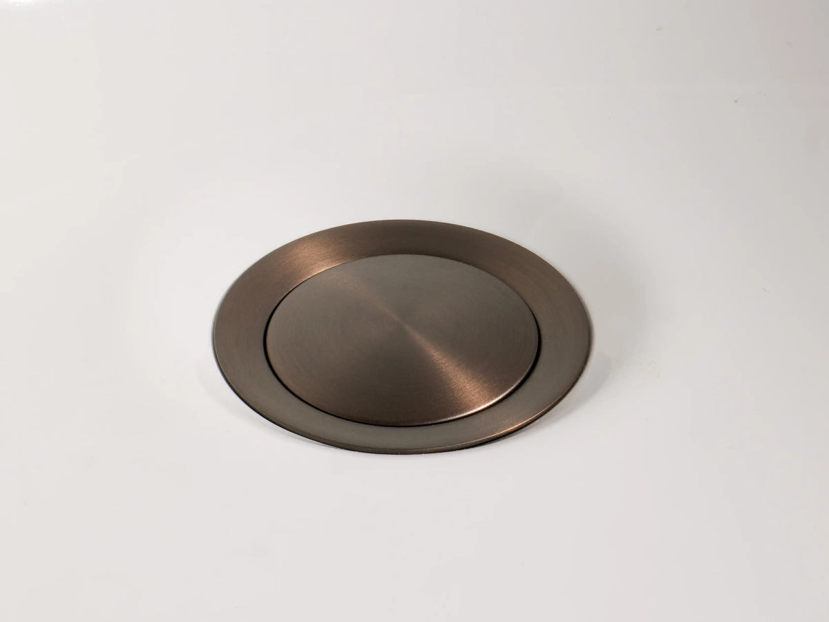 Crewe Smooth Faucet handle with a horizontal bar and cylindrical base, in antique bronze on white marble.