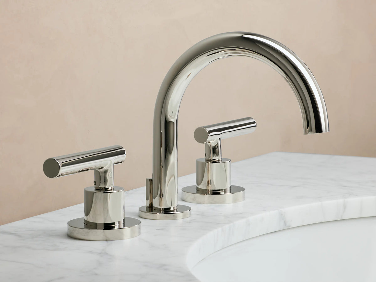 Polished nickel Crewe Smooth Faucet with curved spout and two cylindrical handles, mounted on a marble countertop.