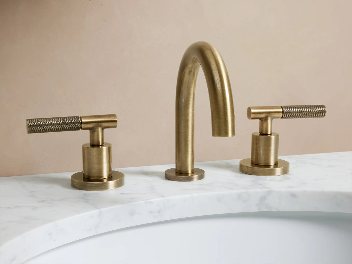 Crewe Knurled Faucet in antique brass finish shown installed on a marble countertop with two side handles and curved spout.