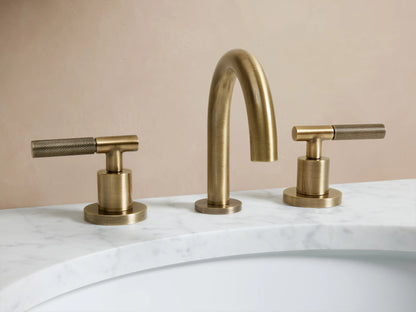 Crewe Knurled Faucet in antique brass finish shown installed on a marble countertop with two side handles and curved spout.